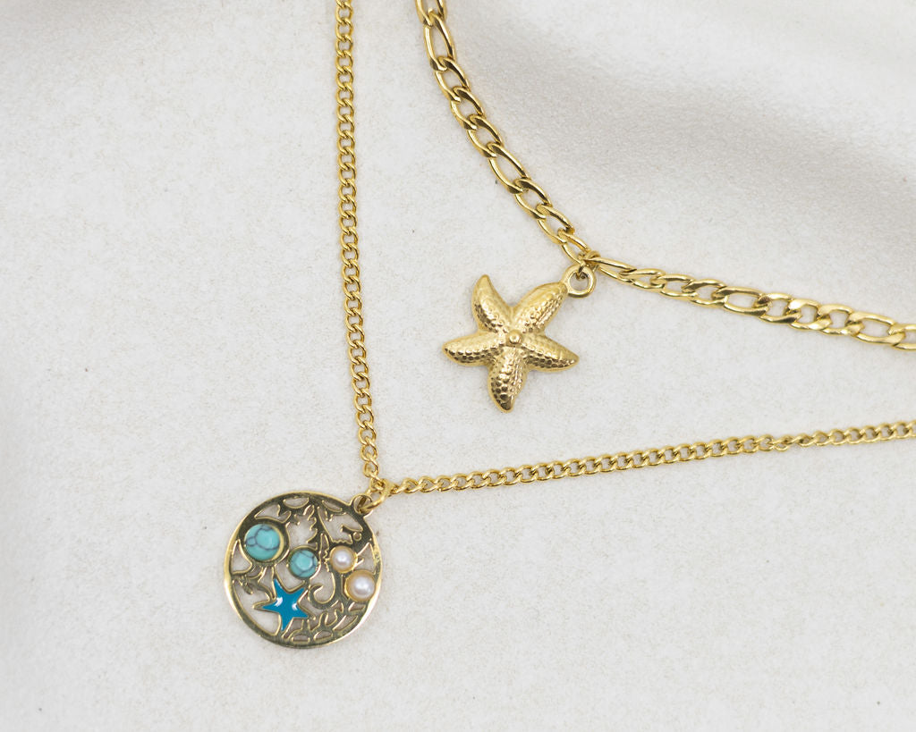 Gold necklace with starfish and circular pendant on a white background