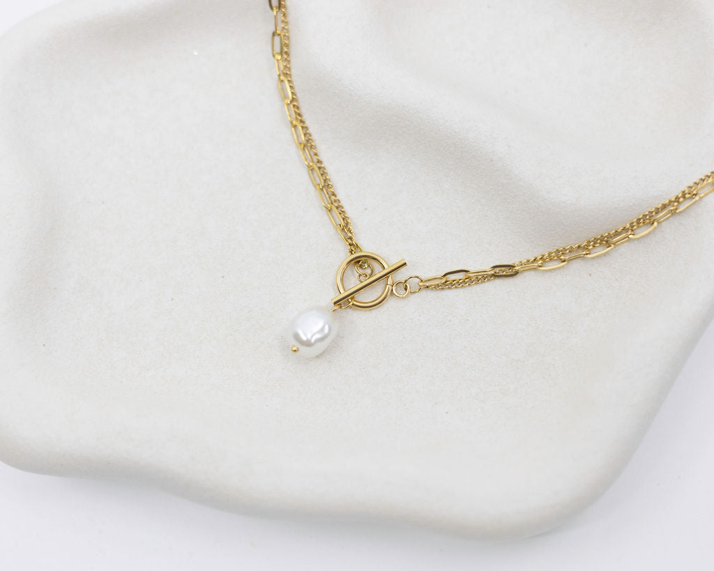 Gold necklace with a pearl pendant on a white surface
