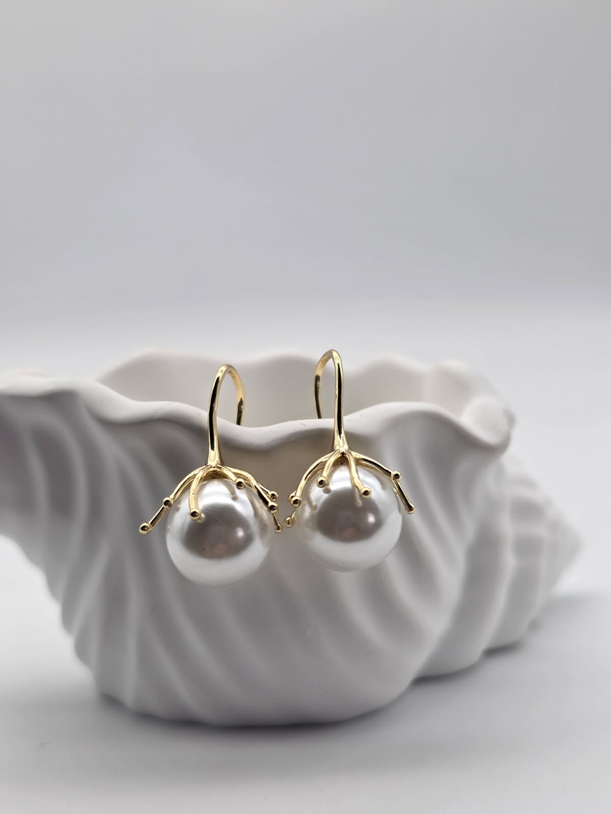 Pearl earrings with gold hooks on a white shell against a light gray background