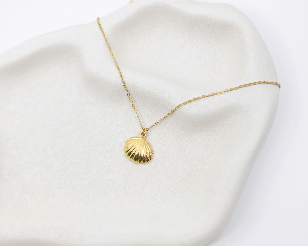 Gold necklace with a shell pendant on a white fabric background