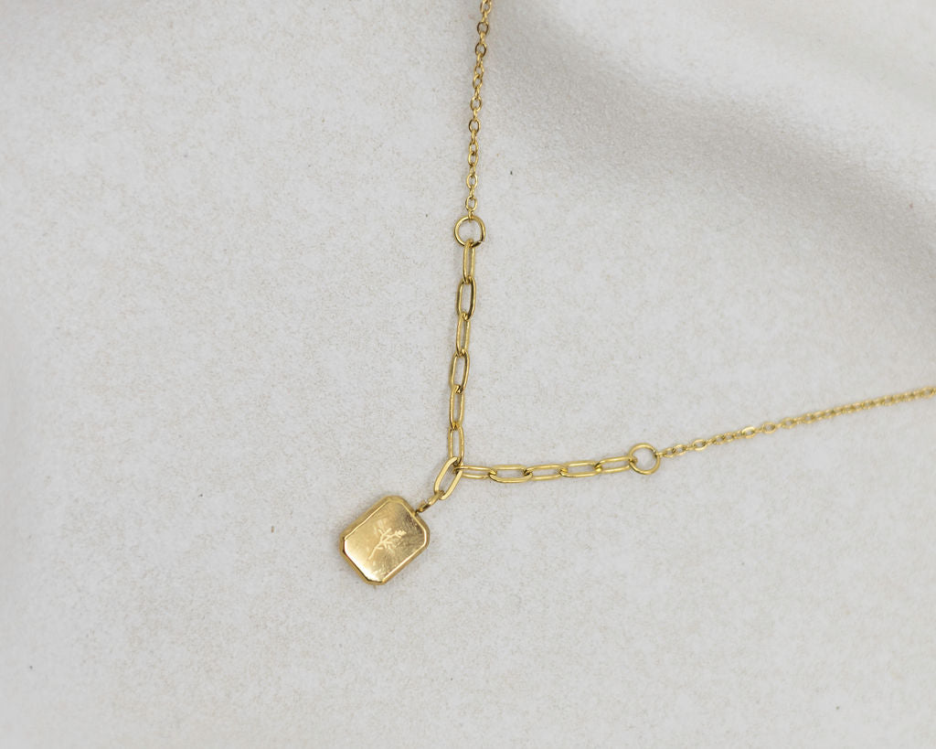 Gold necklace with a small pendant on a light gray background