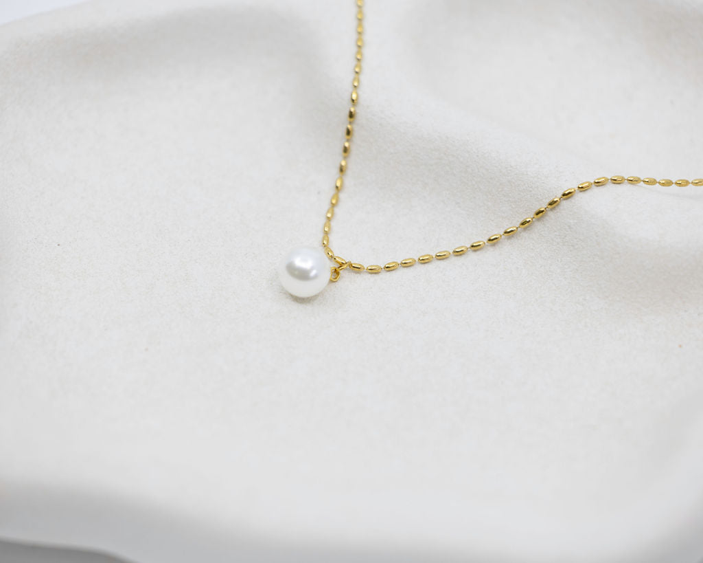 gold chain necklace with round pearl drop on white background