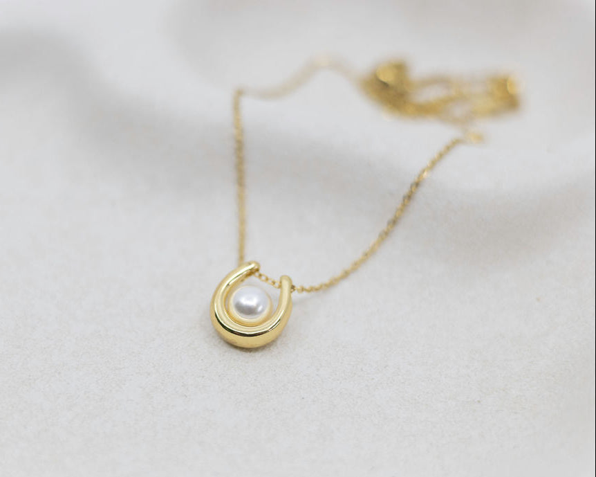 Gold necklace with a pearl pendant on a light background