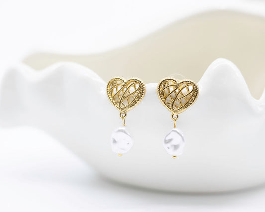 Gold heart-shaped earrings with pearl drops on a white dish