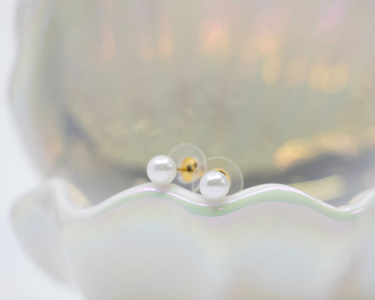 Pearl earrings displayed on a shell with a white background