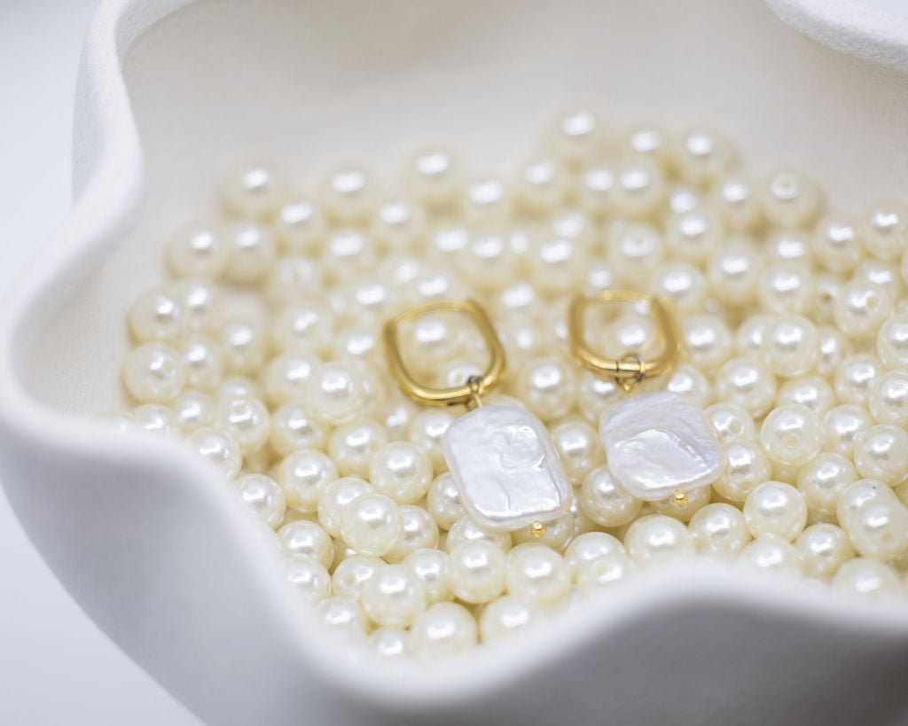 Pearl earrings with gold accents on a bed of pearls in a white dish.