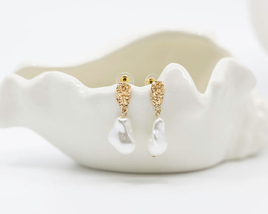 Gold earrings on a white ceramic dish with a plain background