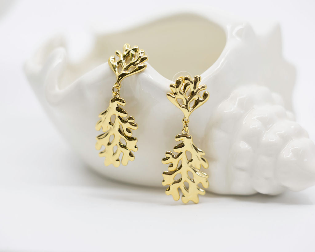 Gold coral-shaped earrings on a white ceramic dish