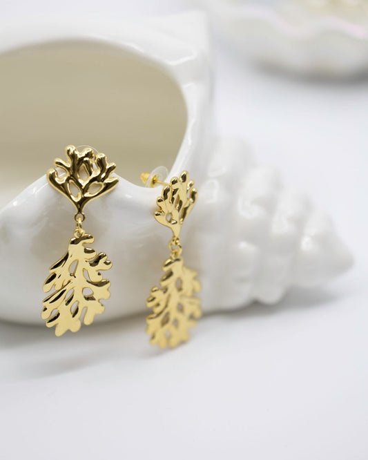 Gold coral shaped earrings on a white shell background