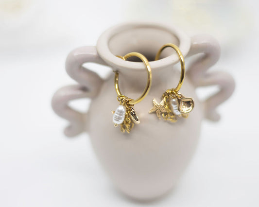 Gold hoop earrings with charms on a white ceramic holder