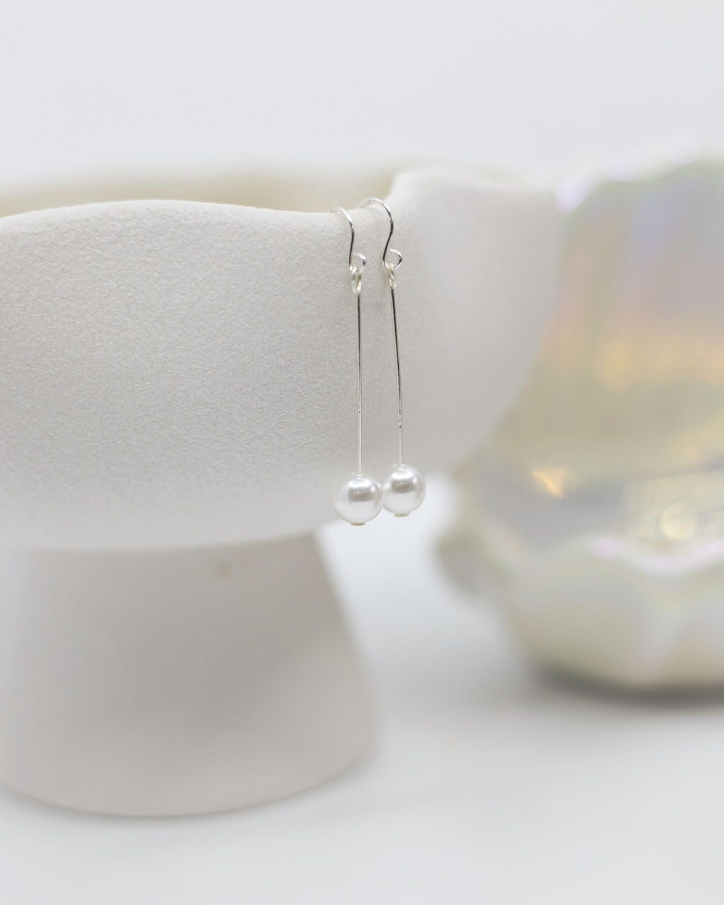 Pearl earrings hanging from a shell on a white background