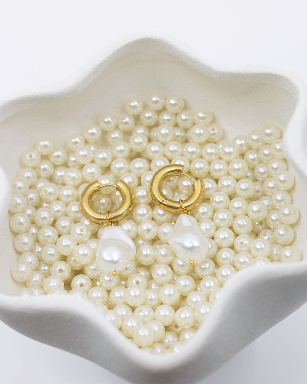 Gold hoop earrings on a bed of pearls in a white dish
