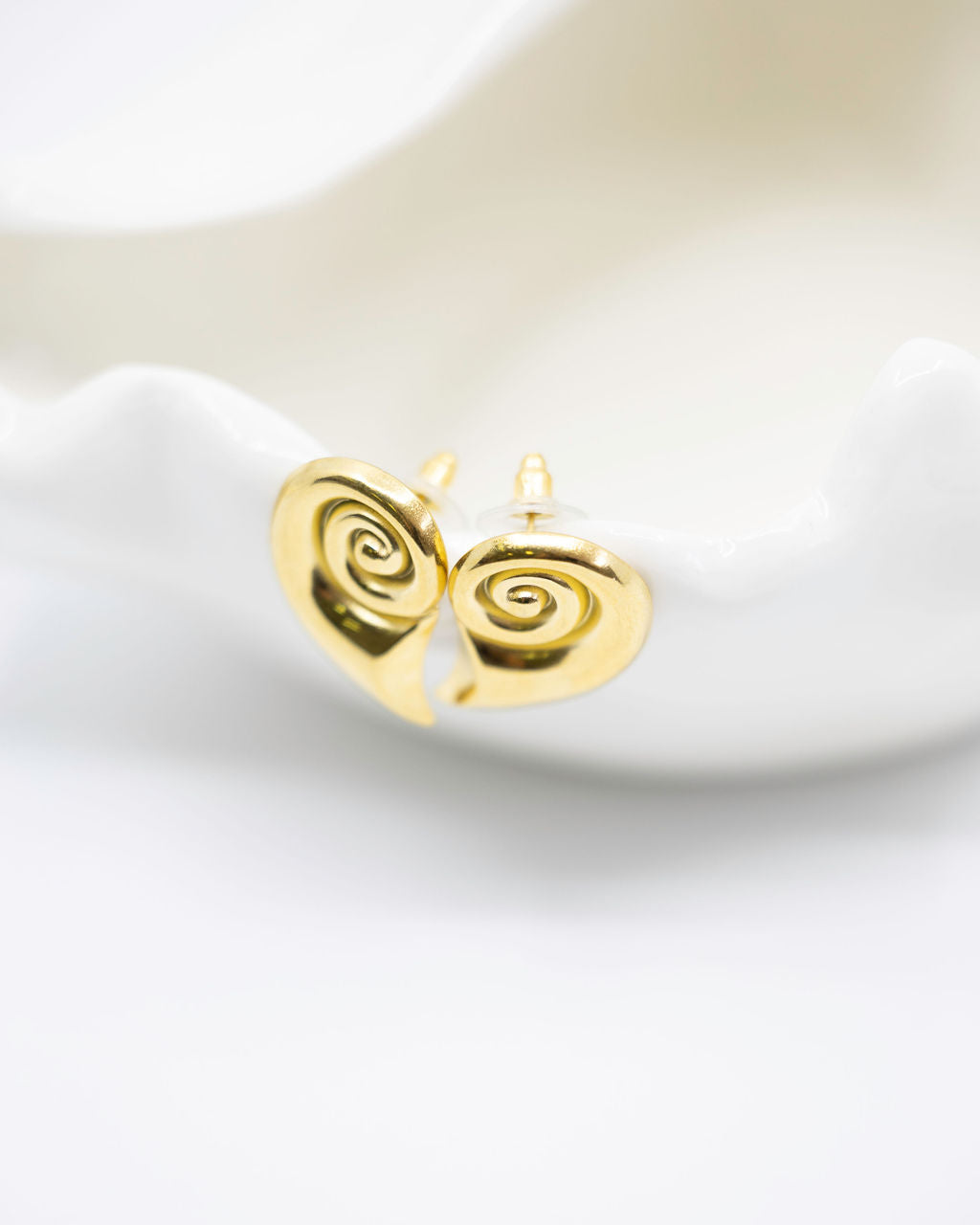 gold spiral shell earrings on white dish