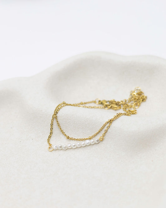 Gold necklace with pearls on a white surface