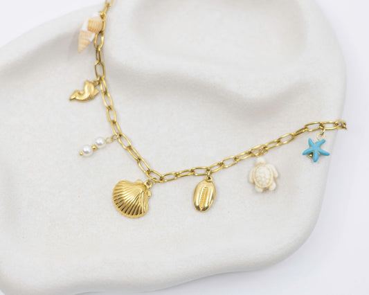 Gold necklace with shell and starfish charms on a white surface