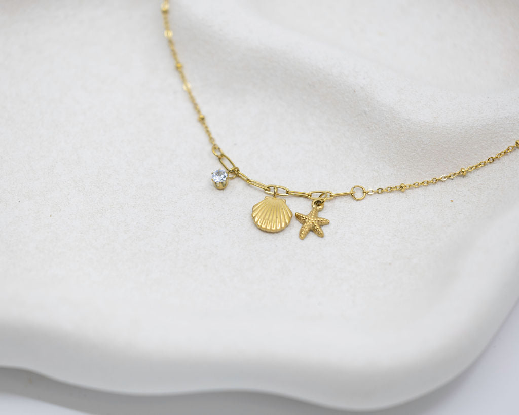Gold necklace with shell and starfish charms on a white fabric background