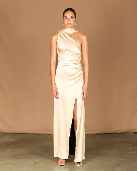 Woman wearing a beige one-shoulder gown with a slit on a brown background