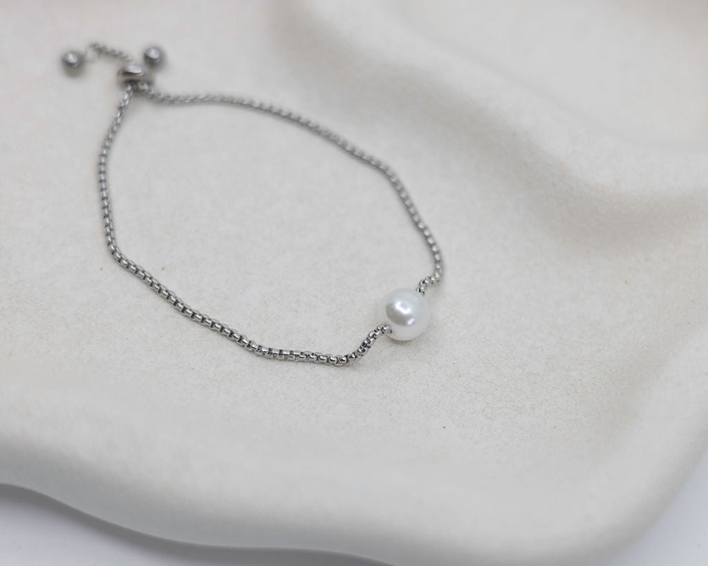 Silver bracelet with a single pearl on a soft white background