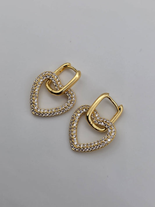 Gold heart-shaped earrings with clear stones on a gray background