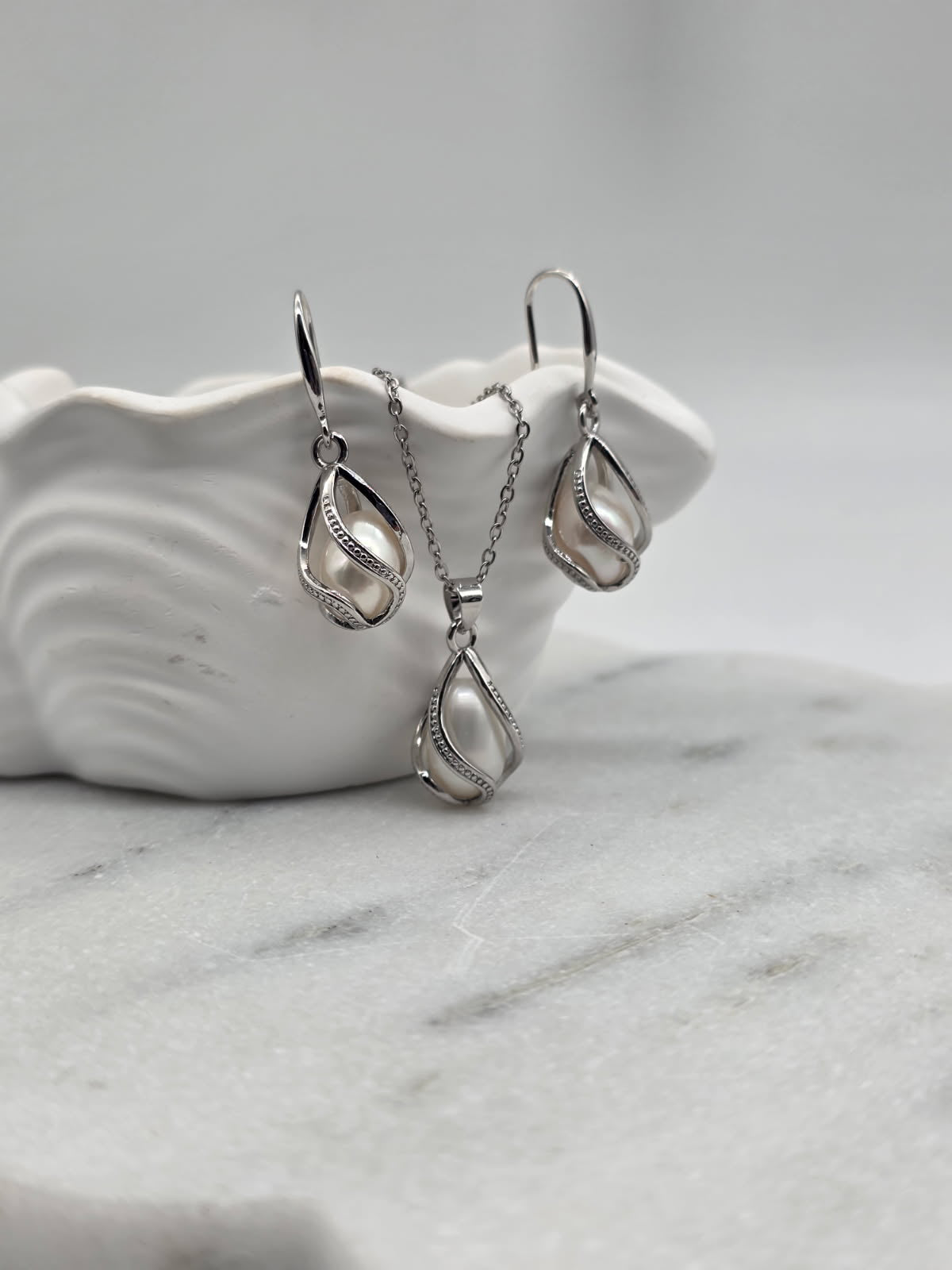 Silver teardrop pendant and earrings on a white ceramic dish with a marble surface.
