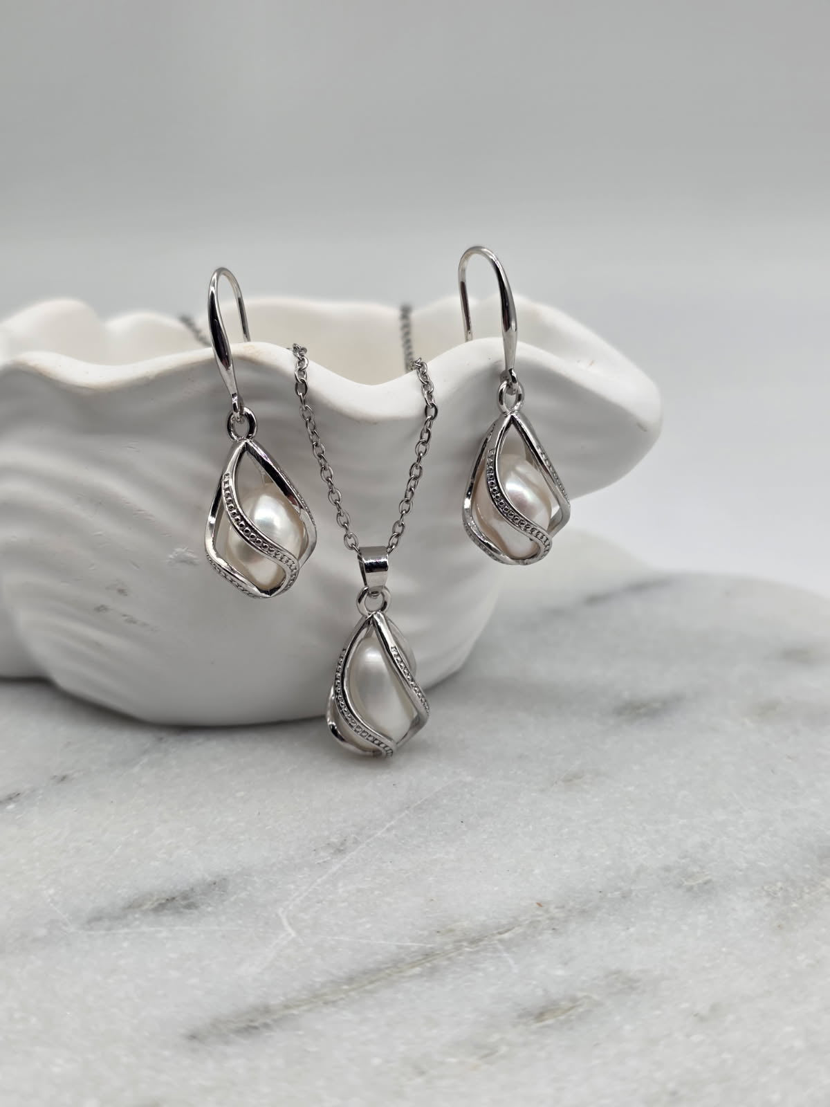 Silver teardrop necklace and earrings on a white shell with a marble background