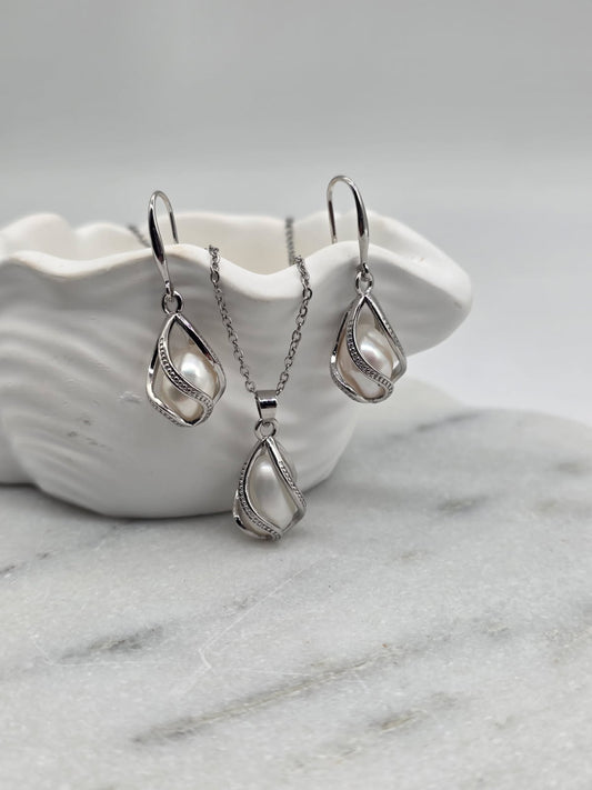 Silver teardrop necklace and earrings on a white shell with a marble background
