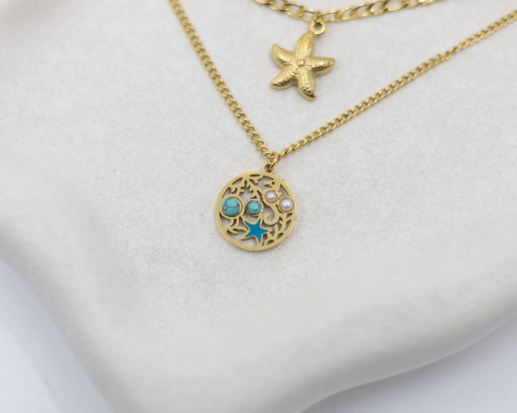 Gold necklace with starfish and circular pendant on a white background
