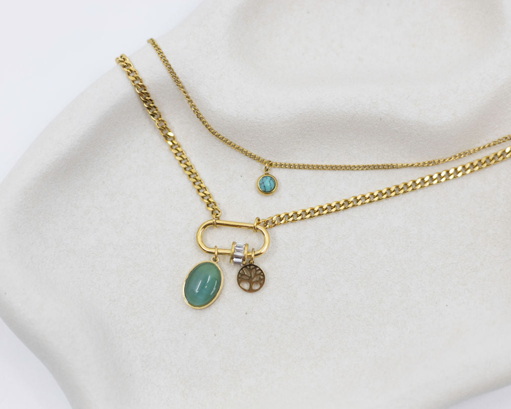 Two gold necklaces with green gemstones on a white surface