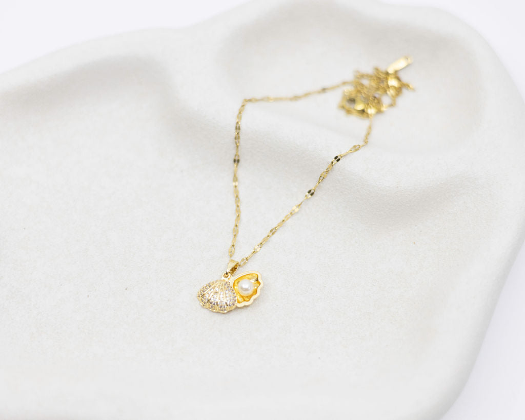 Gold necklace with a clam-shaped pendant on a white background