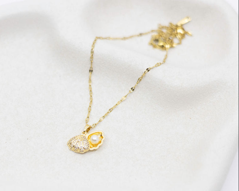 Gold necklace with a clam-shaped pendant on a white surface