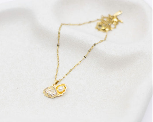 Gold necklace with a clam-shaped pendant on a white surface
