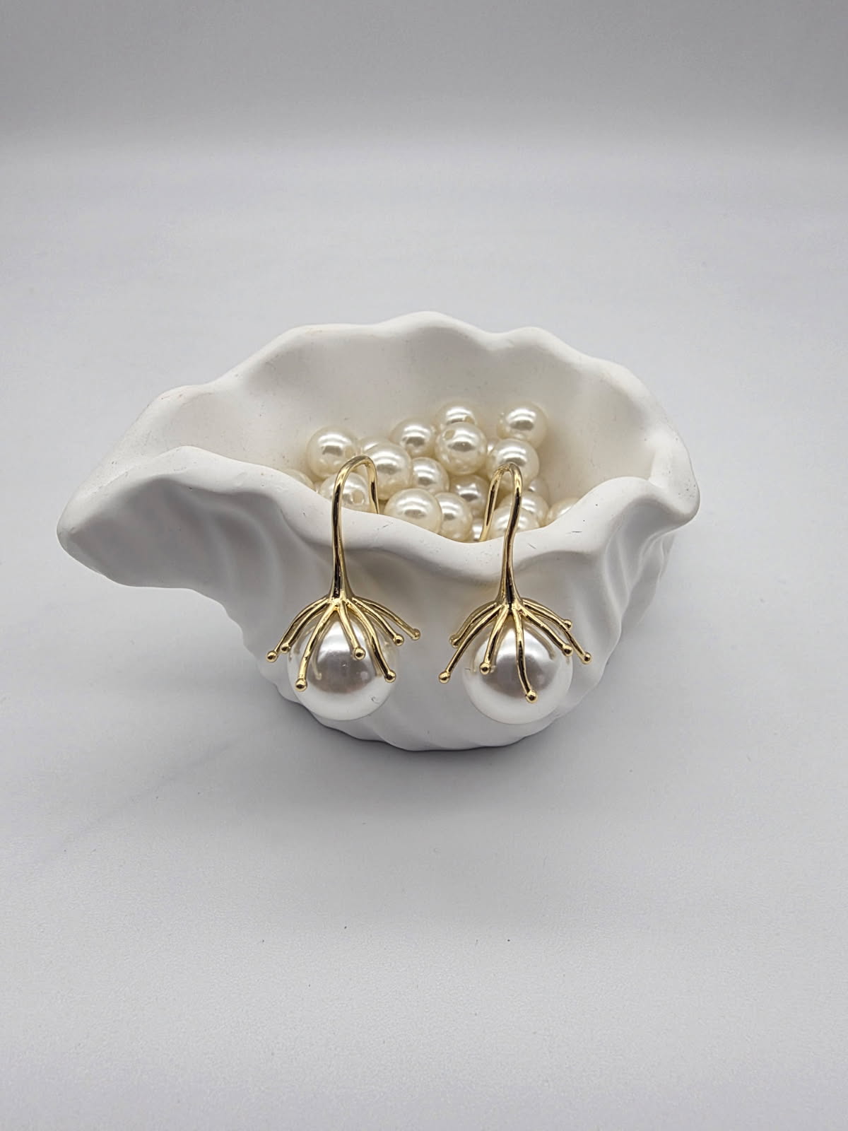 Pearl earrings with gold stems in a white shell on a light gray background