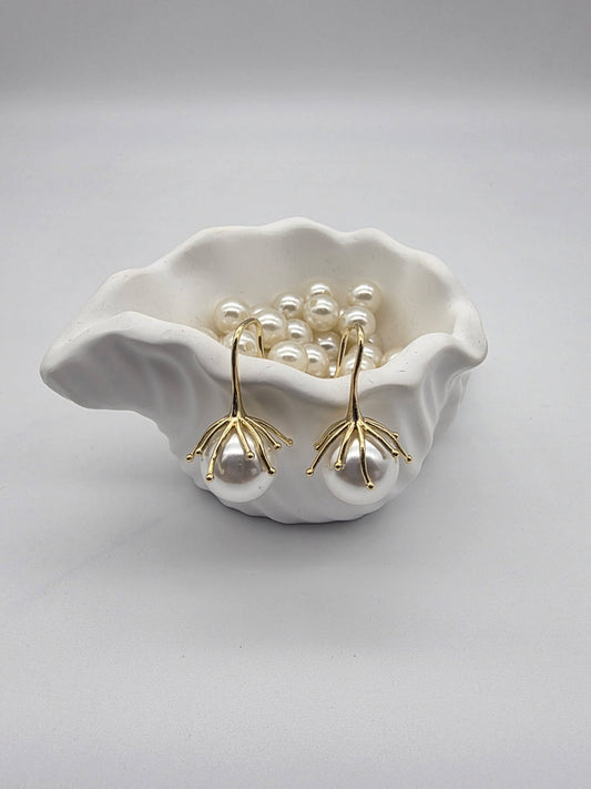 Pearl earrings with gold stems in a white shell on a light gray background