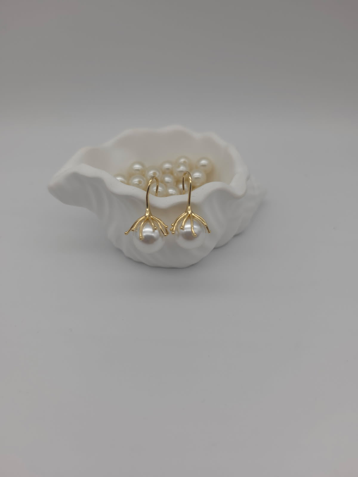 Gold earrings with pearls on a white ceramic dish against a light gray background