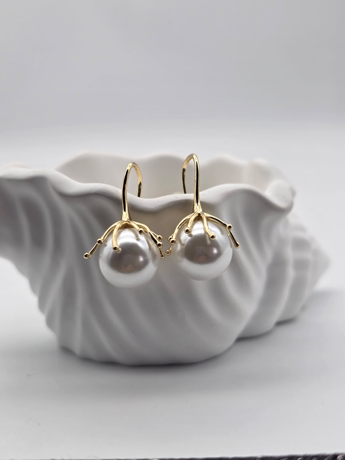 Pearl earrings with gold accents on a white shell-shaped dish