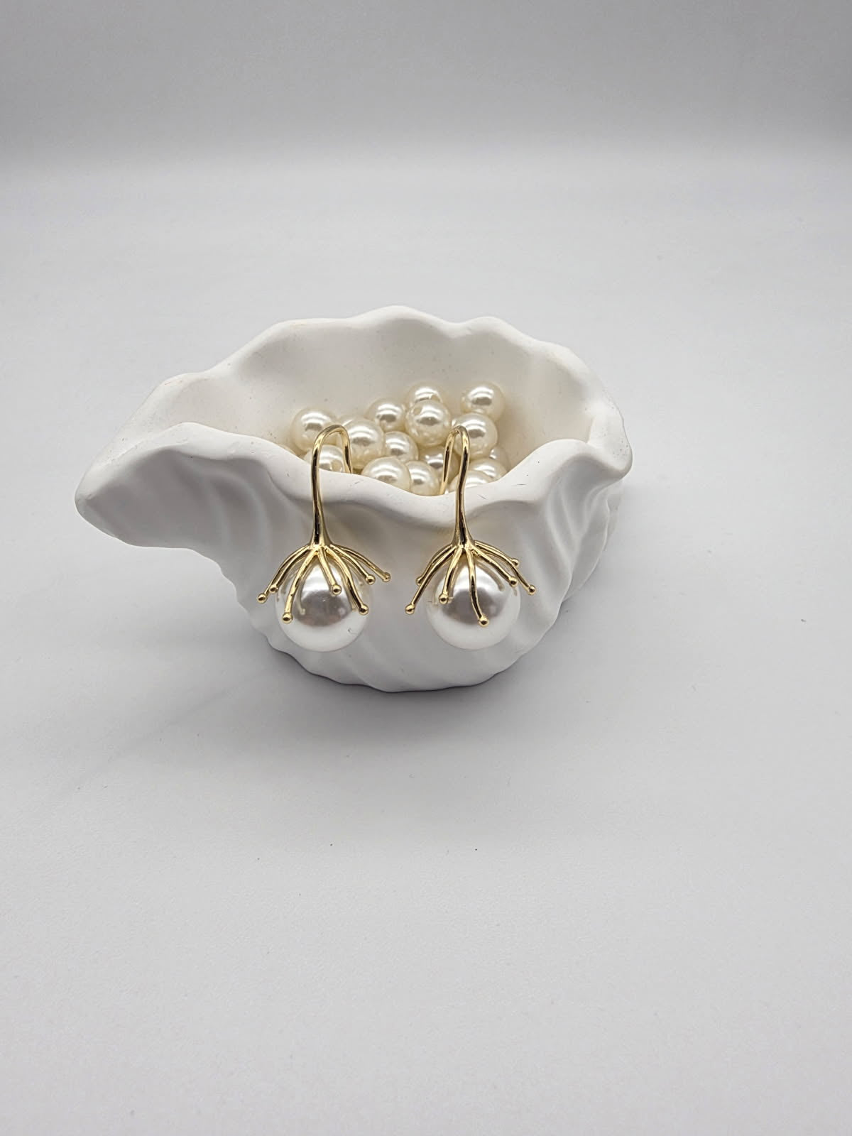 Pearl earrings in a white shell dish on a light gray background