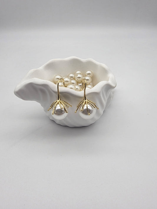 Pearl earrings in a white shell dish on a light gray background