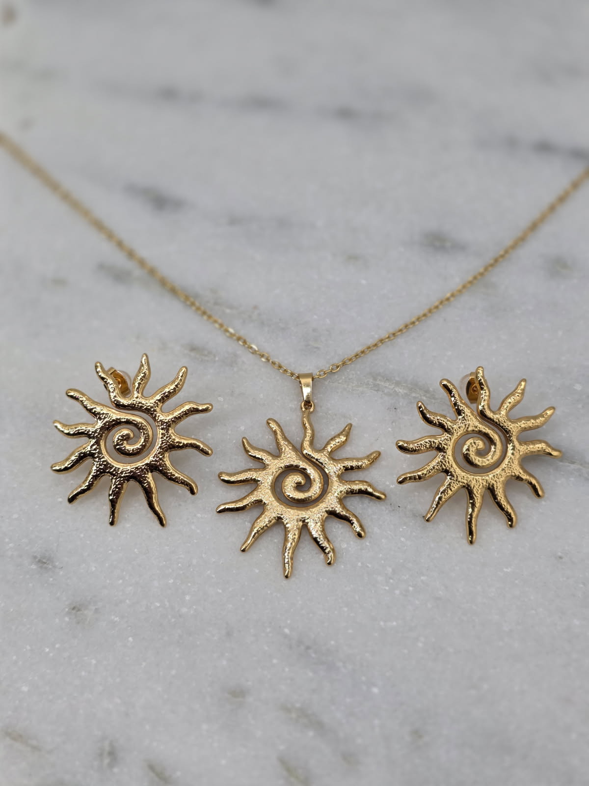 Three sun-shaped gold pendants on a marble surface
