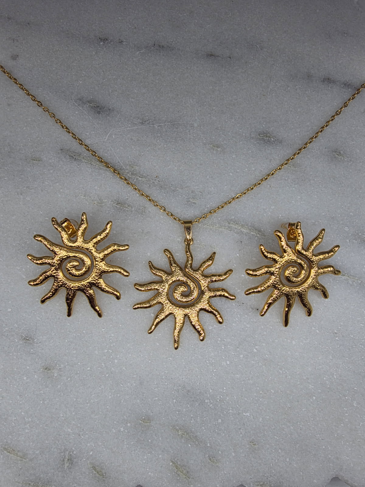 Gold sun-shaped jewelry set on a marble surface