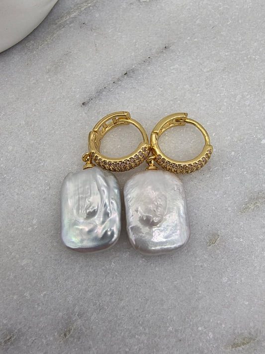 Gold hoop earrings with large pearl-like stones on a marble surface