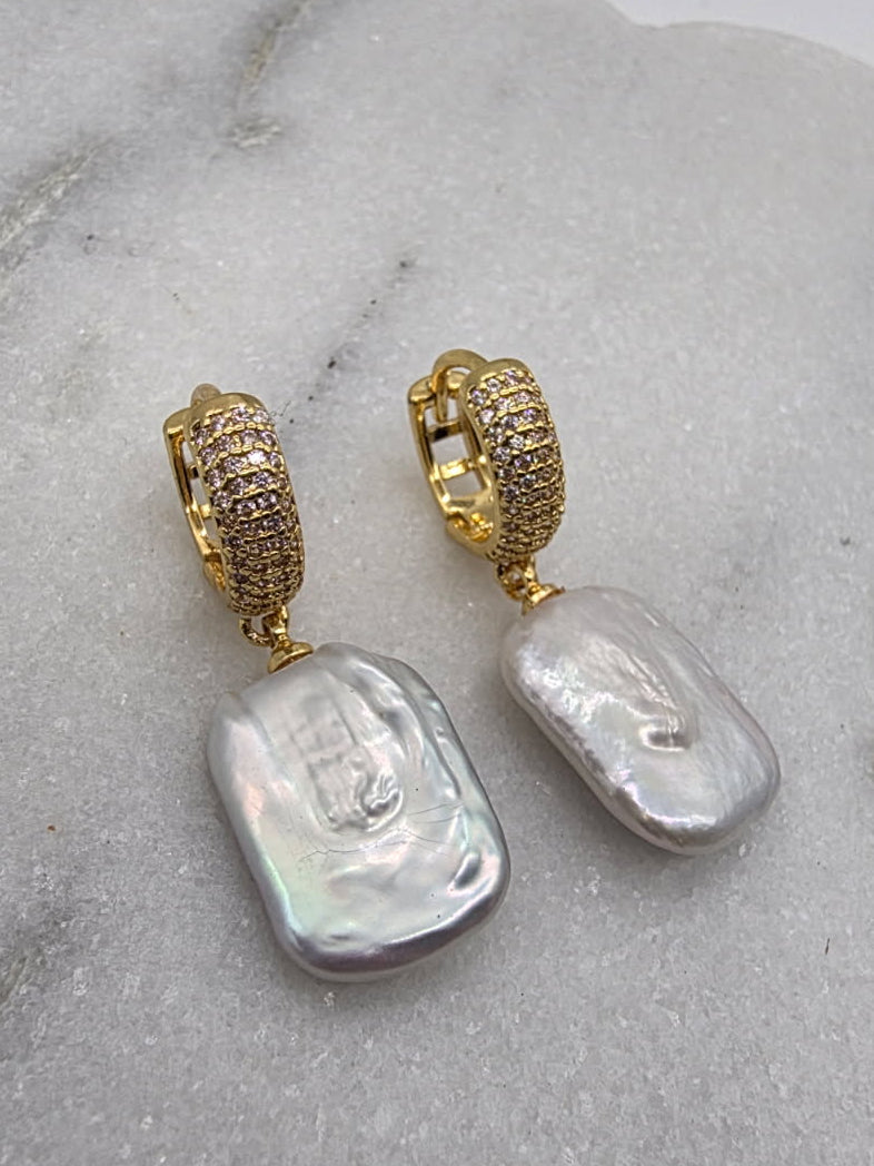 Pair of earrings with gold tops and baroque pearl drops on a marble surface