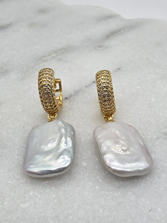 Gold hoop earrings with large white stones on a marble surface