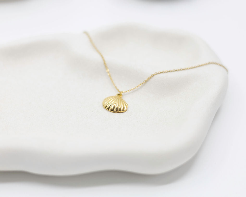 Gold necklace with a shell pendant on a white surface