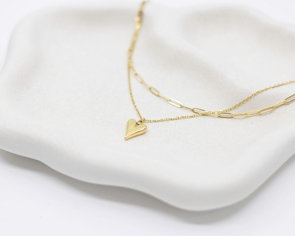 Gold necklace with a heart pendant on a white cushion