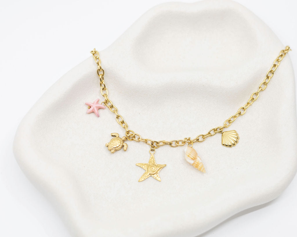 Gold bracelet with star, turtle, and shell charms on a white dish