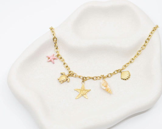 Gold bracelet with star, turtle, and shell charms on a white dish