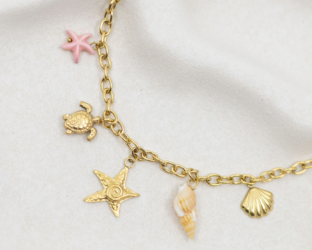 Gold bracelet with turtle, starfish, shell, and pink starfish charms on a white background