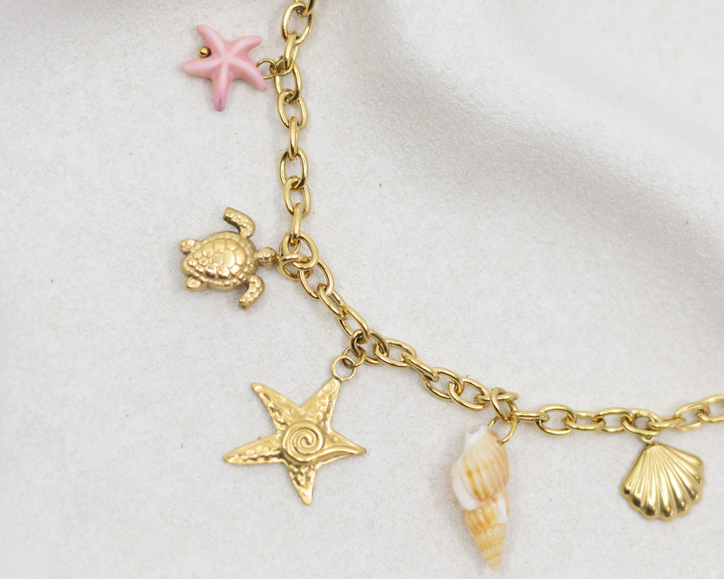 Gold charm bracelet with turtle, starfish, and shell charms on a white background