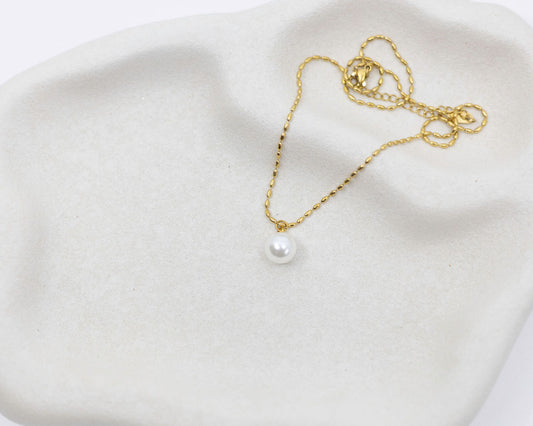 gold chain necklace with round pearl drop on white background