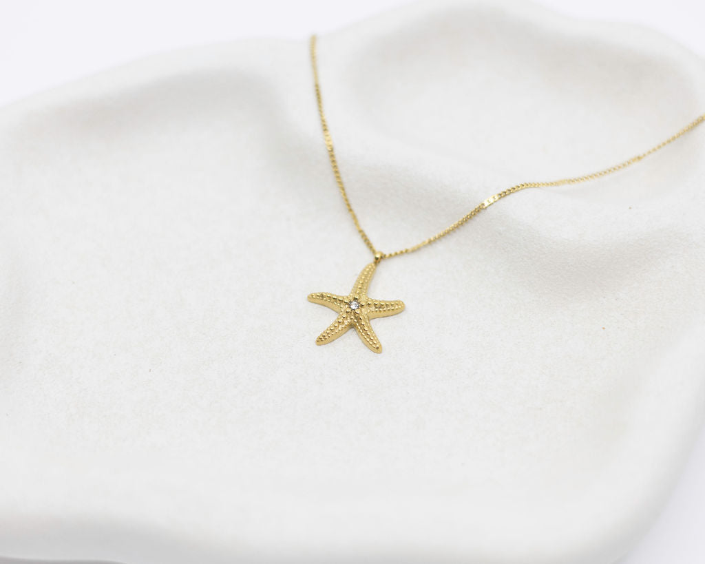 Gold starfish necklace on a white fabric background